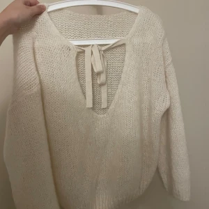 Stickad tröja med rosett - Jättefin stickad tröja med knytband baktill. Tillverkad i Italien med en blandning av akryl, mohair och ull. Aldrig använd, som ny! Vit/beige