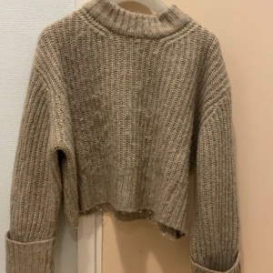 Beige stickad tröja - Säljer en mysig beige stickad tröja med ribbad design. Tröjan har långa ärmar och en croppad passform, perfekt för kyliga dagar. Den har en klassisk rund halsringning och är både stilren och bekväm.