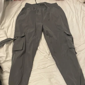 Grå cargobyxor  - Säljer ett par grå cargobyxor i storlek M. Byxorna har elastisk midja med snörning och flera praktiska fickor på sidorna. Perfekta för en avslappnad stil. Använd fåtal gånger!