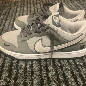 Grå Nike sneakers - Snygga grå Nike sneakers med vit sula och svart Nike-logga. Skorna har snörning och är tillverkade i mocka och syntetmaterial. Perfekta för en stilren look.