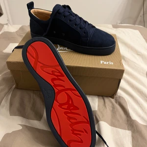Mörkblå Christian Louboutins - Snygga mörkblå sneakers från Christian Louboutin med den ikoniska röda sulan. Skorna har en stilren design med snörning och är tillverkade i mocka. Perfekta för att ge en lyxig touch till din outfit. Dom har en liten defect som syns på den sista bilden. Meddela vid intresse pris kan diskuteras!