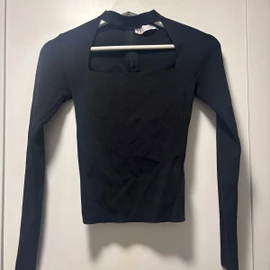 Svart långärmad topp från Zara - Snygg svart långärmad topp från Zara med en unik fyrkantig öppning vid halsen. Perfekt för en stilren look. Tillverkad i ett stretchigt material för en bekväm passform.