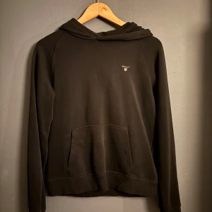 Svart hoodie från Gant - Säljer en stilren svart hoodie från Gant med en klassisk känguruficka framtill. Den är köpt från Kids Brand Store för några månader sedan och är i ett bra skick. Nypris 599, hör av dig vid funderingar🙌