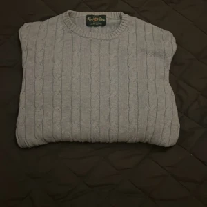 Ljus blå stickad tröja  - Säljer en klassisk blå stickad tröja från Alan Paige Tröjan har ett stilrent kabelstickat mönster och rund halsringning. Perfekt för kyliga dagar.