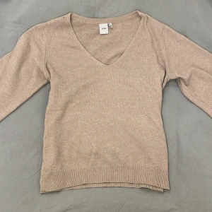 Beige tröja från ICHI - Säljer en stilren beige tröja från ICHI med v-ringning. Tröjan har långa ärmar och ribbade kanter vid ärmslut och nederkant. Perfekt för en avslappnad look.