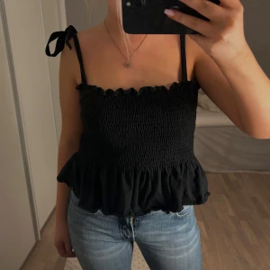 Svart  topp med volang - Säljer denna söta svarta topp med volangdetalj och knytband på axlarna.  Storlek S 