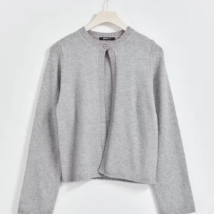 Grå kofta med knappdetalj💞 - Säljer en stilren grå kofta med rund hals och knappdetalj framtill. Perfekt för lager-på-lager och passar till många olika outfits. Koftan har långa ärmar och ribbade kanter för en klassisk look.