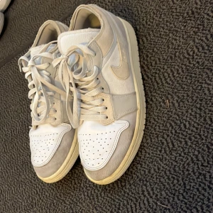 Air Jordan 1 Low SE Craft - Säljer ett par Nike sneakers i vitt och beige med snörning. Skorna har en klassisk design med perforerade detaljer på tån och en bekväm sula.