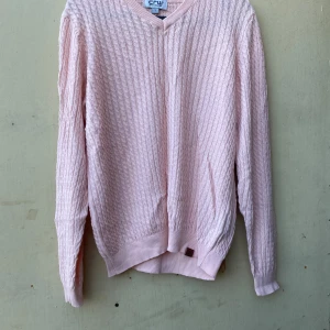 Ljusrosa stickad tröja från CRW - Säljer en superfin ljusrosa stickad tröja från CRW. Den har en snygg v-ringning och är perfekt för både höst och vår. Tröjan är långärmad och har ett diskret kabelstickat mönster som ger den en klassisk look. Perfekt för en mysig dag ute eller hemma!