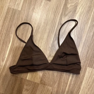 Brun ribbad bikiniöverdel - En snygg brun ribbad bikiniöverdel i trekantsmodell. Den har smala axelband och en enkel design som passar perfekt för sommaren. Materialet känns mjukt och bekvämt mot huden. Inte använd! Storlek M