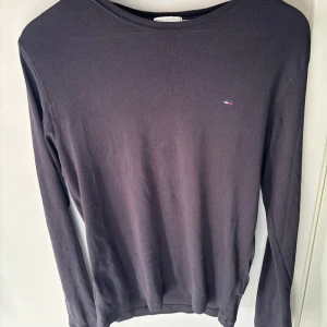 Svart långärmad tröja från Hilfiger Denim - Säljer en stilren svart långärmad tröja från Hilfiger Denim. Tröjan har en liten broderad logga på bröstet och är perfekt för både vardag och lite finare tillfällen. Den är i storlek M och gjord av mjukt material som känns skönt mot huden.🔥