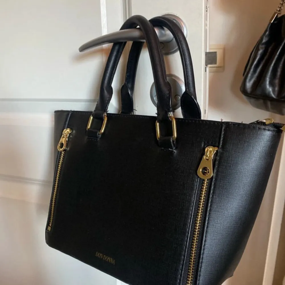 Säljer en snygg svart handväska från don Donna . Väskan har en stilren design med två dekorativa dragkedjor på framsidan och bekväma handtag. Perfekt för både vardag och fest! pris kan diskuteras vid snabb affär!💋. Laukut & Käsilaukut.
