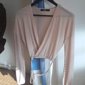 Beige omlottopp från Bik Bok - Säljer en superfin beige omlottopp från Bik Bok. Den har långa ärmar och en snygg v-ringning. Perfekt för både vardag och fest! 💫