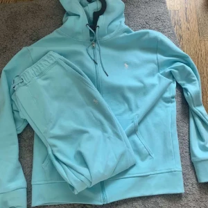 Ljusblå hoodie från Ralph Lauren - Säljer en superfräsch ljusblå hoodie från Ralph Lauren. Den har en dragkedja framtill och är gjord i mjukt bomullsmaterial. Perfekt för en chill dag eller när du vill vara bekväm men ändå snygg. Den har långa ärmar och en liten broderad logga på bröstet. Passar perfekt till våren eller hösten!
