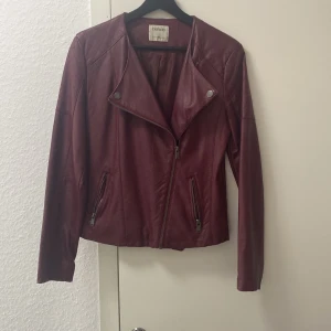 Vinröd skinnjacka från DeFacto - Säljer en snygg vinröd skinnjacka från DeFacto. Jackan har en cool asymmetrisk dragkedja och två fickor med dragkedjor framtill. Den är långärmad och har en stilren design med knappar på kragen. Perfekt för höst och vår!