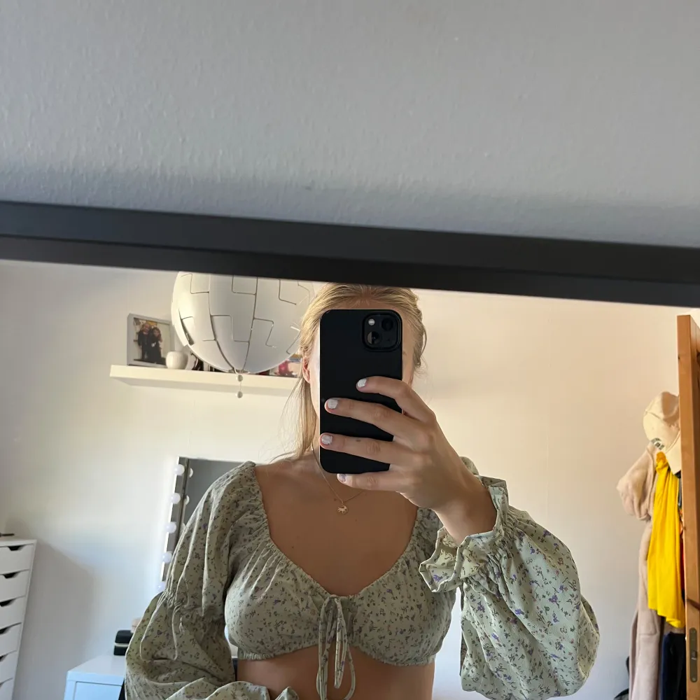 Ljusgrön blommig kort blus, knyte i mitten och resårer mitt på armar. Endast använd 1 gång 💚. Puserot.