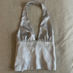 Ljusblå halterneck topp - Fest topp/linne i ljusblått satin. Knyte i ryggen, som går att knyta som man vill. Lite mindre i storlek. Helt oanvänd!