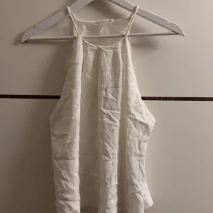 Vit ärmlös topp med spetsdetaljer - Säljer en superfin vit ärmlös topp med spetsdetaljer. Perfekt för sommardagar eller en festlig kväll. Toppen har en luftig passform och tunna axelband. Den är både stilren och elegant, vilket gör den lätt att matcha med olika outfits.