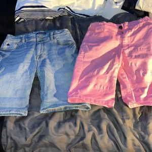 Två par shorts i jeans och rosa tyg - Säljer två par shorts, ett par i klassiskt blått jeansmaterial och ett par i härligt rosa tyg från DNG. Perfekta för sommaren! Jeansshortsen har en avslappnad passform med fickor och knappdetaljer. De rosa shortsen är också bekväma och stilrena. Båda paren är i bra skick och redo för nya äventyr! 🌞