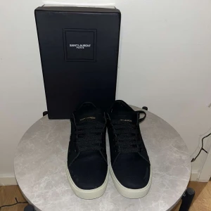Svarta sneakers från Saint Laurent - Snygga svarta sneakers från Saint Laurent i mycket bra skick. De har en klassisk design med vit sula och diskret Saint Laurent-logga på sidan. Perfekta för både vardag och fest. Kommer med originalförpackning.