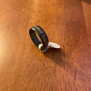 Svart ring med text - Säljer en stilren svart ring med ingraverad text 'forever love'. Perfekt för vardagsbruk eller som en meningsfull present. Ringen har en enkel och modern design. Storlek 21mm