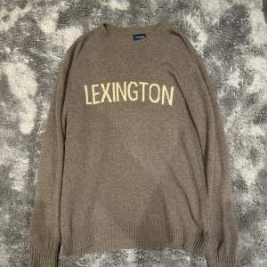 Säljer en snygg beige stickad tröja från Lexington. Den har en klassisk design med texten 'LEXINGTON' i vitt på framsidan. Tröjan är långärmad och perfekt för kyliga dagar. Passar både till vardags och lite finare tillfällen. Supermysig och stilren!