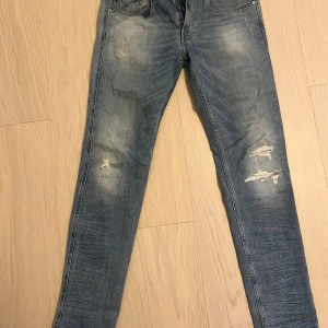 Blå jeans från Replay - Säljer ett par snygga blå jeans från Replay i modellen Anbass. De har en slim passform och är i bra skick med coola slitningar på framsidan. Perfekta för en avslappnad stil och kan bäras året runt. Passar både till vardags och fest!