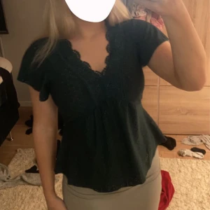 Mörkgrön topp med spetsdetaljer - Säljer en söt mörkgrön topp med spetsdetaljer och korta ärmar. Toppen har en vacker v-ringning och ett fint mönster som ger en romantisk känsla. Perfekt för både vardag och fest!