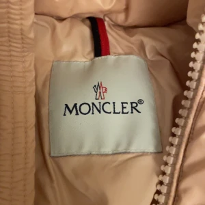 Oanvänd ljus rosa dunjacka från Moncler - Säljer en superfin ljusrosa dunjacka från Moncler. Passar storlek S och M. Den är perfekt för kalla dagar med sin pufferstil och dragkedja framtill. Jackan har en hög krage och praktiska fickor med knappar. Den är i mycket bra skick och redo för vintern! 💖❄️