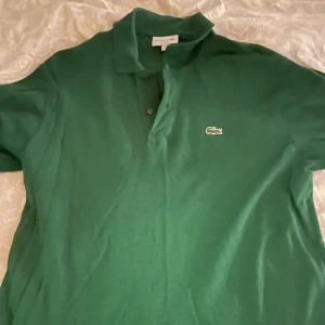 Grön pikétröja från Lacoste - Säljer en klassisk grön pikétröja från Lacoste i storlek L. Tröjan har den ikoniska krokodilloggan på bröstet och är i ett bekvämt bomullsmaterial. Perfekt för både vardag och lite mer uppklädda tillfällen. Passar bra till både jeans och chinos!