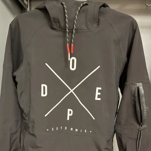 Svart jacka från Dope - Säljer en svart jacka från Dope i mycket bra skick. Den har en cool design med tryck på framsidan och dragkedjor på ärmarna. Insidan är fodrad med mjuk fleece för extra värme. Perfekt för nästa skidresa.