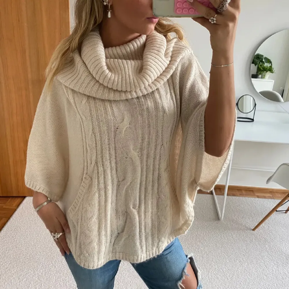 Superfin beige stickad poncho med en stor polokrage som ger en mysig känsla. Perfekt för höst och vinter, den har ett snyggt flätmönster framtill och är i ett löst passande snitt. Perfekt att slänga över en t-shirt eller långärmad tröja för extra värme. 🧣✨. Tröjor & Koftor.