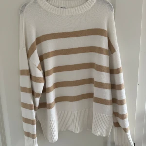 Stickad randig tröja - Säljer en superfin randig tröja i storlek S. Den är vit med beige ränder och har en skön, stickad känsla. Slits i sidan och mudd i kanterna. Använd fåtal gånger. Mycket fint skick!💗