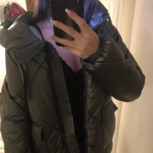 Grönglansig quiltad pufferjacka med huva - Säljer en snygg grönglansig pufferjacka i quiltad stil. Jackan har en huva och dragkedja framtill. Perfekt för kalla höst- och vinterdagar. Den är i mycket bra skick och har en normal passform. Supermysig och trendig!