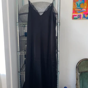 Svart klänning med spetsdetaljer - Säljer en elegant svart klänning med spetsdetaljer vid halsringningen. Klänningen har en smickrande passform. Perfekt för festliga tillfällen eller en utekväll.