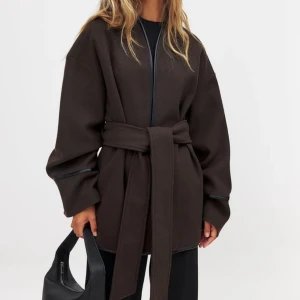 Brun kappa med bälte NA-KD - Slutsåld brun kortare kappa från NA-KD. Helt oanvänd med lapparna kvar, inga egna bilder då den aldrig använts utan enbart testats. Ligger kvar i påsen den kom i. Hann inte skicka tillbaka den därför säljer jag den här!