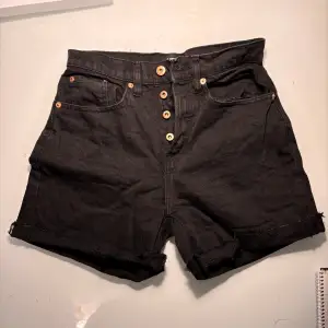 Säljer ett par svarta jeansshorts i bra skick. De är högmidjade med snygga knappar framtill och har en rå kant nertill för en cool look. Perfekta för sommaren eller en avslappnad fest. Passar till det mesta och är superbekväma!