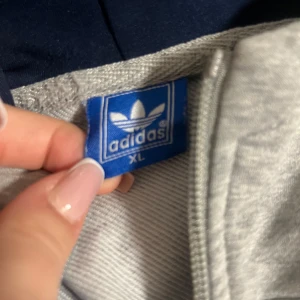 Grå hoodie från Adidas - Säljer en grå hoodie från Adidas i storlek XL. Den har en dragkedja framtill och två fickor. Perfekt för höst och vår, med en klassisk Adidas-logga på bröstet. Superbekväm och stilren! Inga skador alls!💞