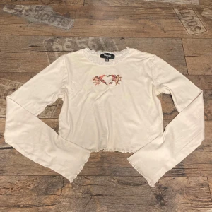 Coquette topp - Säljer en söt vit långärmad topp från NGOrder med ett gulligt änglamotiv och rosor på bröstet. Toppen har spetsdetaljer vid halsringningen💖