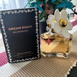 Dream Night Eau So Black Eau de Parfum - Säljer en lyxig parfymflaska från Dream Night med en söt design. Flaskan är dekorerad med vita blommor på korken och har en elegant svart och guld förpackning. Perfekt för kvällar när du vill känna dig extra speciell. Innehåller 100 ml av en förförisk doft.