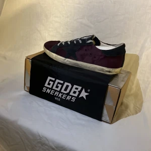 GGDB Sneakers i vinrött och svart - Säljer ett par GGDB sneakers i vinrött och svart. De har en cool, sliten look med vita snören och en svart sula. Perfekta för en avslappnad stil. Skorna är i bra skick och kommer i originalkartong.