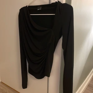 Svart långärmad topp från Gina Tricot - Säljer en elegant svart långärmad topp från Gina Tricot. Den har en draperad design som ger en snygg och stilren look. Perfekt för både vardag och fest. Toppen är i mycket bra skick och redo för en ny garderob!