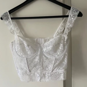 Vit spetskorsett - Säljer en superfin vit spetskorsett med hakknäppning i ryggen. Den har ett vackert blommigt spetsmönster och är perfekt för sommarens fester. Passformen är tight med en snällt tyg mot huden. 