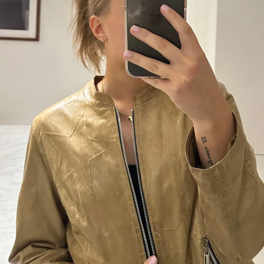 Säljer en snygg beige mockajacka med coola stjärndetaljer. Jackan har en dragkedja framtill och två fickor med dragkedjor. Perfekt för höst och vår, och ger en stilren look. Passar bra till både jeans och klänning!. Jackor.