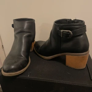 Svarta boots med bälte - Säljer ett par svarta boots  i skinn  med snyggt bälte runt ankeln. De har en robust klack och är perfekta för höst och vinter. Skorna är i bra skick med lite slitage på tån, men fortfarande supertrendiga och bekväma.