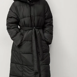 Svart lång pufferjacka med bälte - Säljer en svart lång pufferjacka med bälte i midjan. Jackan har en mysig huva och långa ärmar, perfekt för kalla vinterdagar. Den är både stilren och praktisk, vilket gör den till ett måste i garderoben. Passar perfekt för vinterns alla äventyr! 🖤