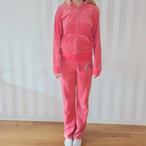 Korall velourset från Juicy Couture - Säljer ett supermysigt korall velourset från Juicy Couture. Setet har en hoodie med dragkedja och långa ärmar, samt matchande byxor. Både tröjan och byxorna har glittriga paljettdetaljer med Juicy Couture-loggan. Storlek L men motsvarar en S