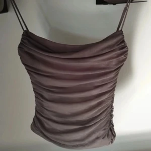 Brun axelbandslös topp från Zara - Säljer en snygg brun axelbandslös topp från Zara i storlek XS. Toppen har en draperad design och sitter korsett liknande. Perfekt för festliga tillfällen eller en utekväll. Knappt använd i jättebra skick. 