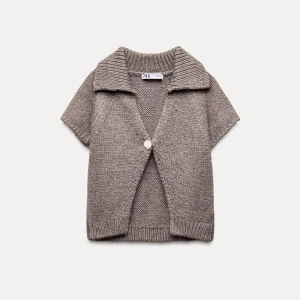 Beige stickad kofta från Zara - Säljer en superfin beige stickad kofta från Zara. Den har korta ärmar och en stor knapp framtill. Perfekt för lager-på-lager under hösten eller våren. Koftan har en mysig och avslappnad stil. Helt ny!!