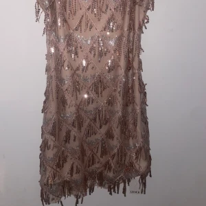 Glittrig champagnefärgad klänning  - Säljer en superfin glittrig klänning i champagnefärg. Den har tunna axelband och är täckt med paljetter i ett snyggt mönster. Perfekt för fest eller nyår! Klänningen är i helt nytt skick och har prislappen kvar 